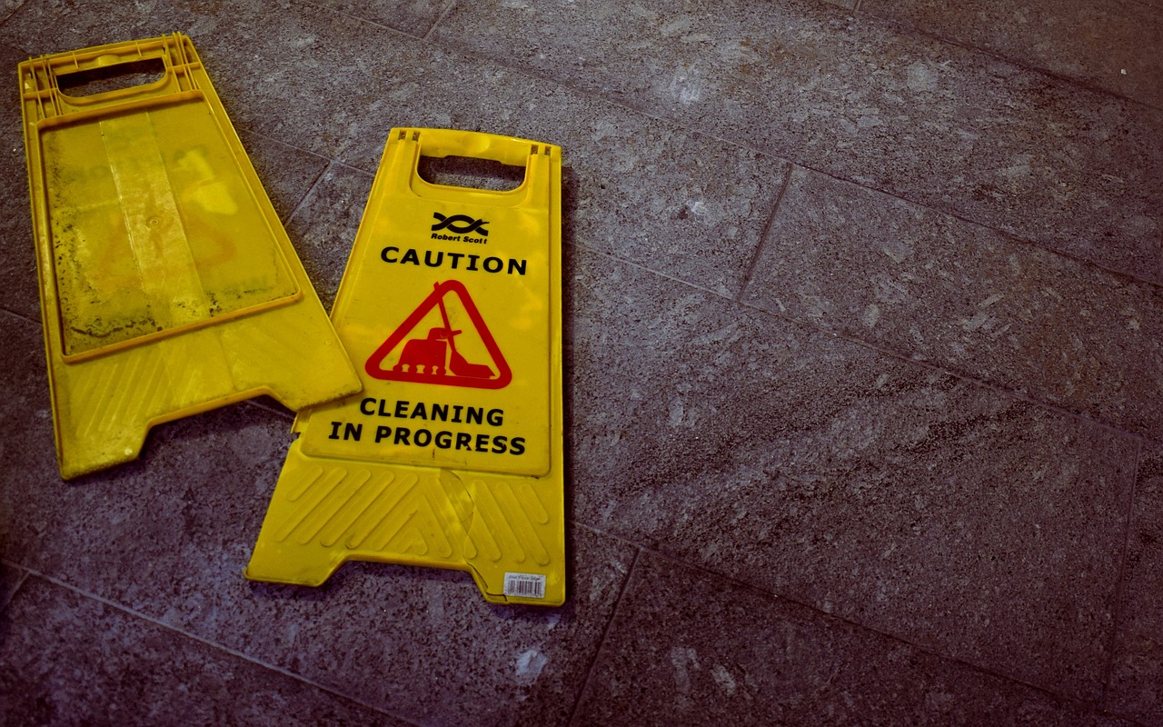 Yellow caution signs on gray tiled floor indicating cleaning in progress.
