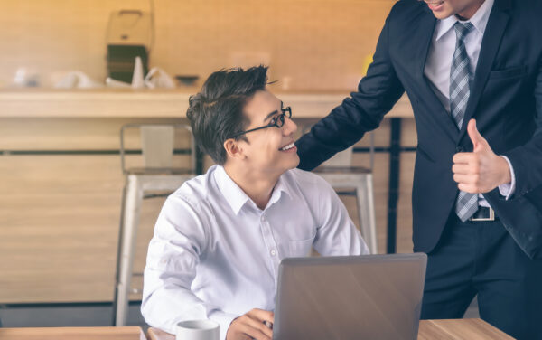 Businessman,Was,Given,A,Thumbs-up,And,Compliments,From,His,Boss Business colleagues sharing success, one seated with a laptop, while the other gives a thumbs-up gesture.