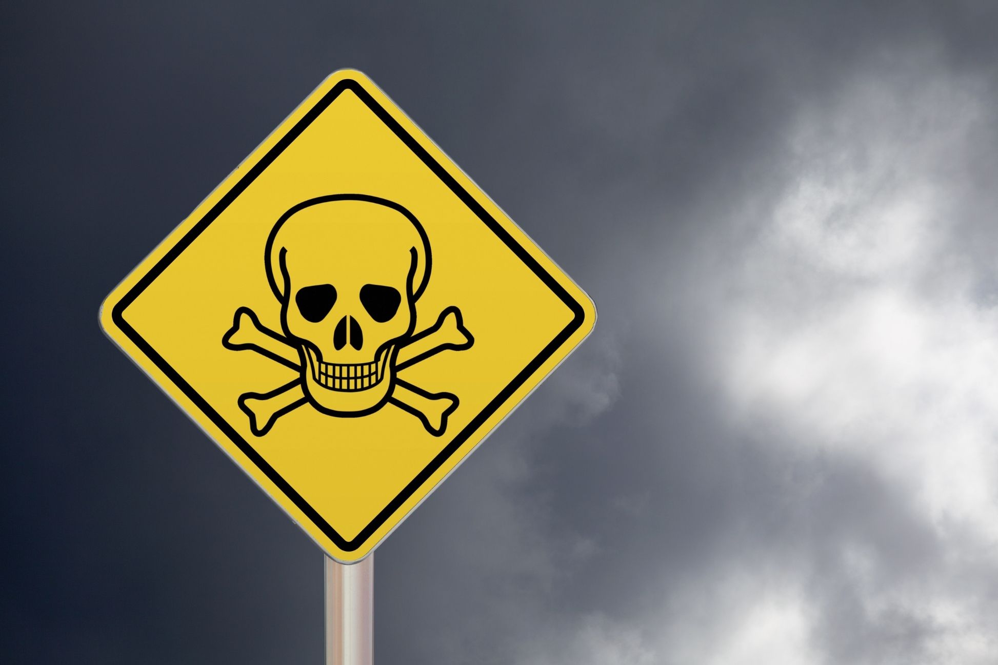 Yellow warning sign with skull and crossbones against a cloudy sky, indicating danger or toxic area.