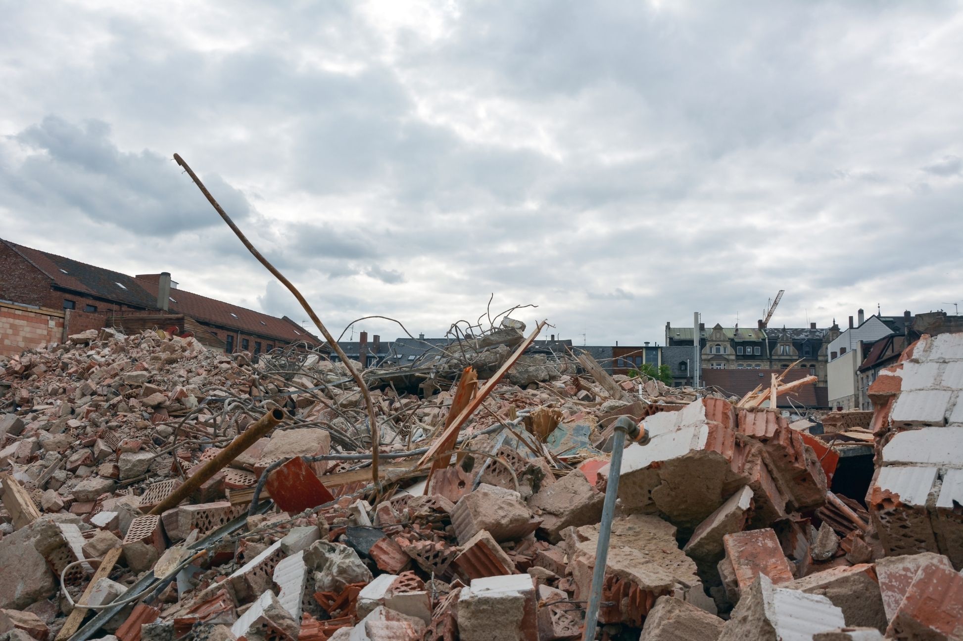 Urban demolition site with broken bricks and debris under a cloudy sky.