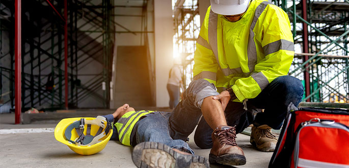 Construction worker injured on site, receiving first aid. Safety helmet and gear visible. Workplace accident response.