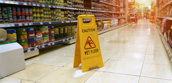 Yellow Caution Wet Floor sign in a grocery store aisle with shelves of canned goods.