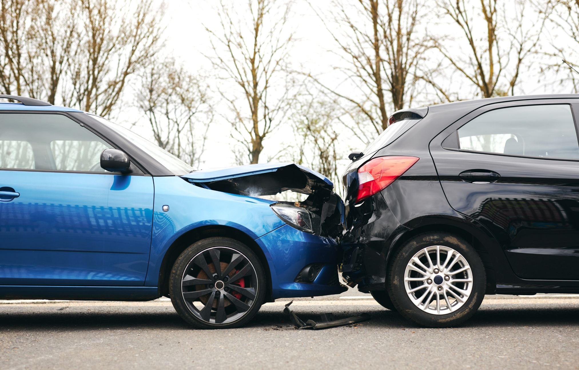 Two cars in a rear-end collision, a blue car hitting a black one, with visible damage to both.
