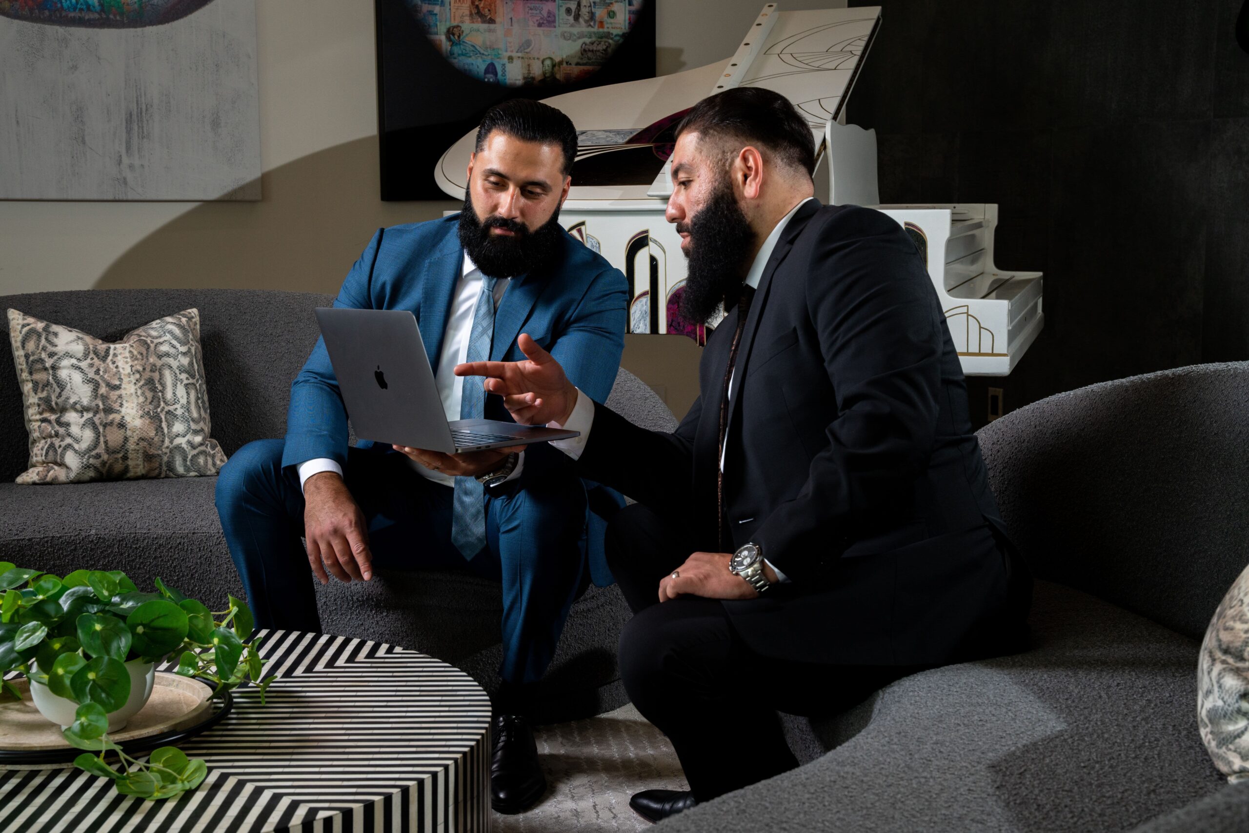 Two men in suits discussing work on a laptop in a stylish office setting with modern decor.