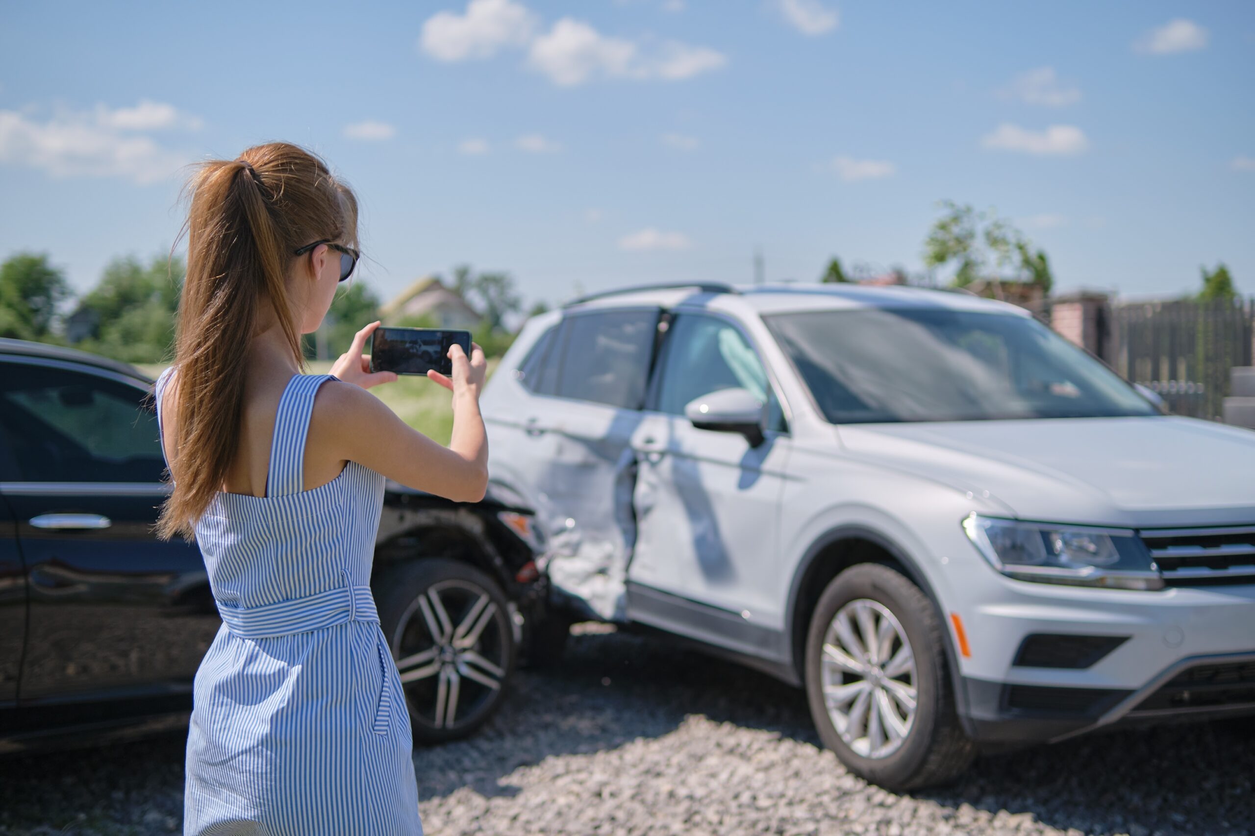 Woman photographing car accident damage with smartphone outdoors.