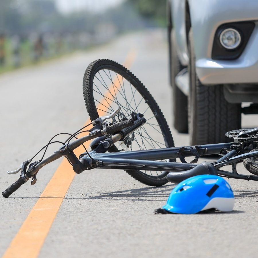 Bicycle accident scene with bike and helmet on road beside car, implying collision.