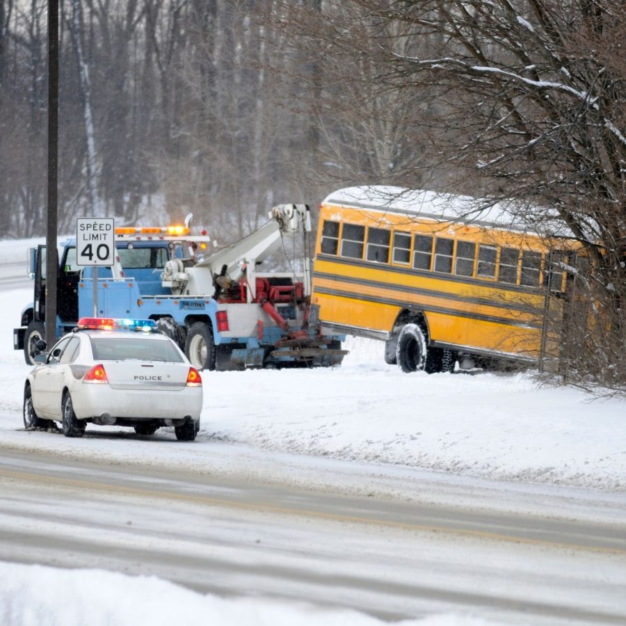 Police and tow truck assist yellow school bus stuck in snow by roadside, winter scene.