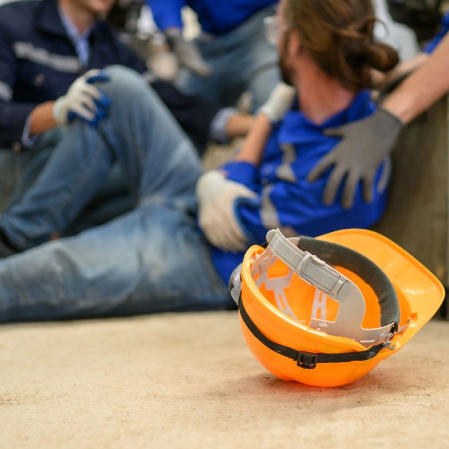 Worker receiving aid on construction site with hard hat in foreground. Workplace safety concept.