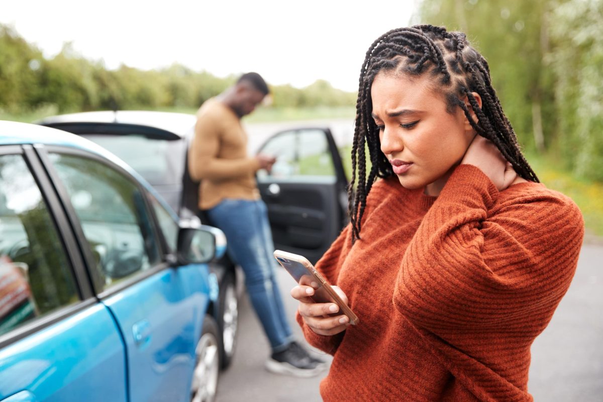 Two people near cars after an accident, one looking concerned on her phone, the other standing by a car door.