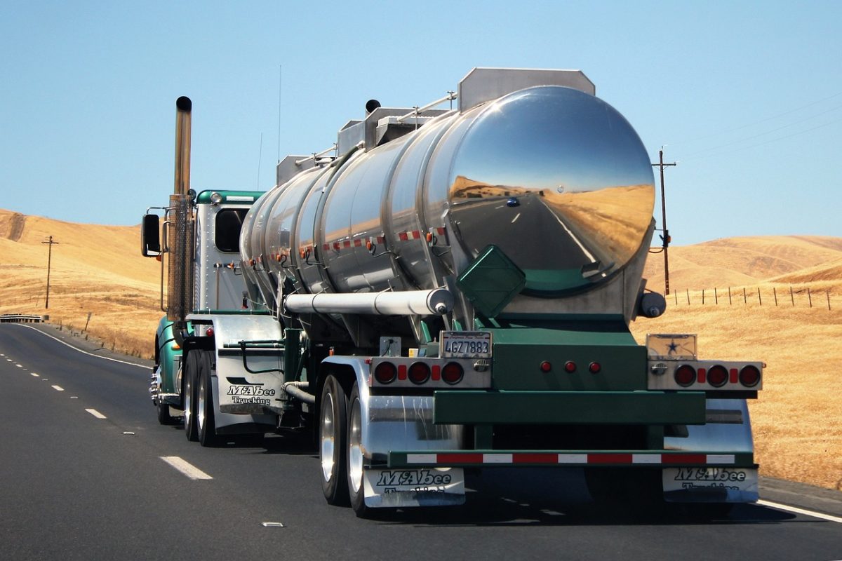 Tanker truck on highway with hills in background reflecting on metal surface.