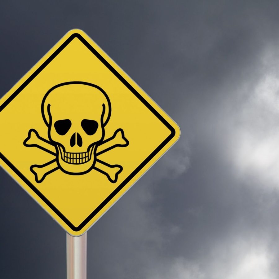 Yellow warning sign with skull and crossbones against a cloudy sky, indicating danger or toxic area.