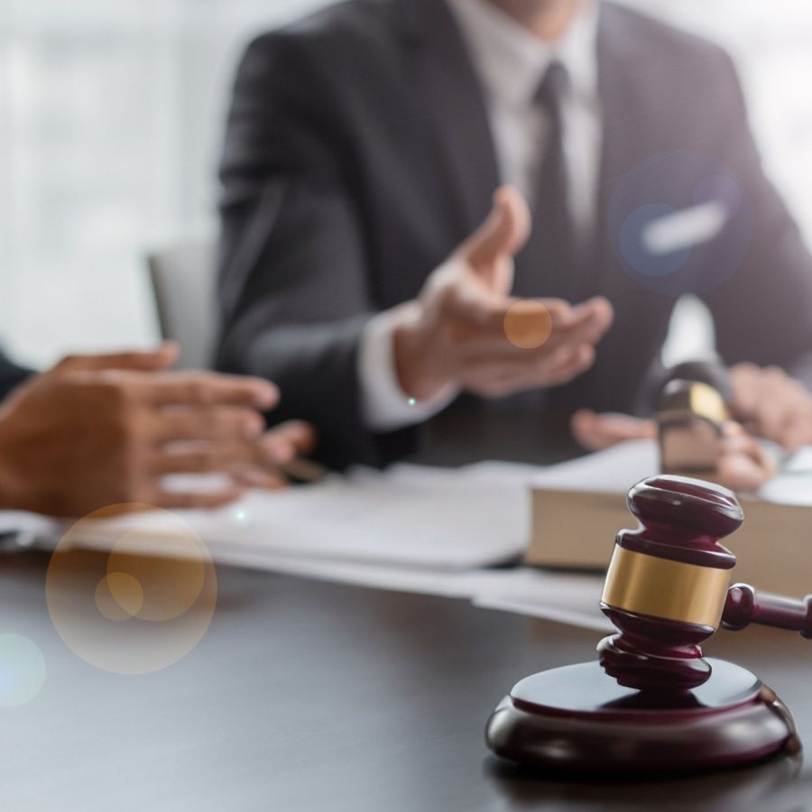 Gavel on a table in a law office meeting, with attorneys discussing legal documents in the background.