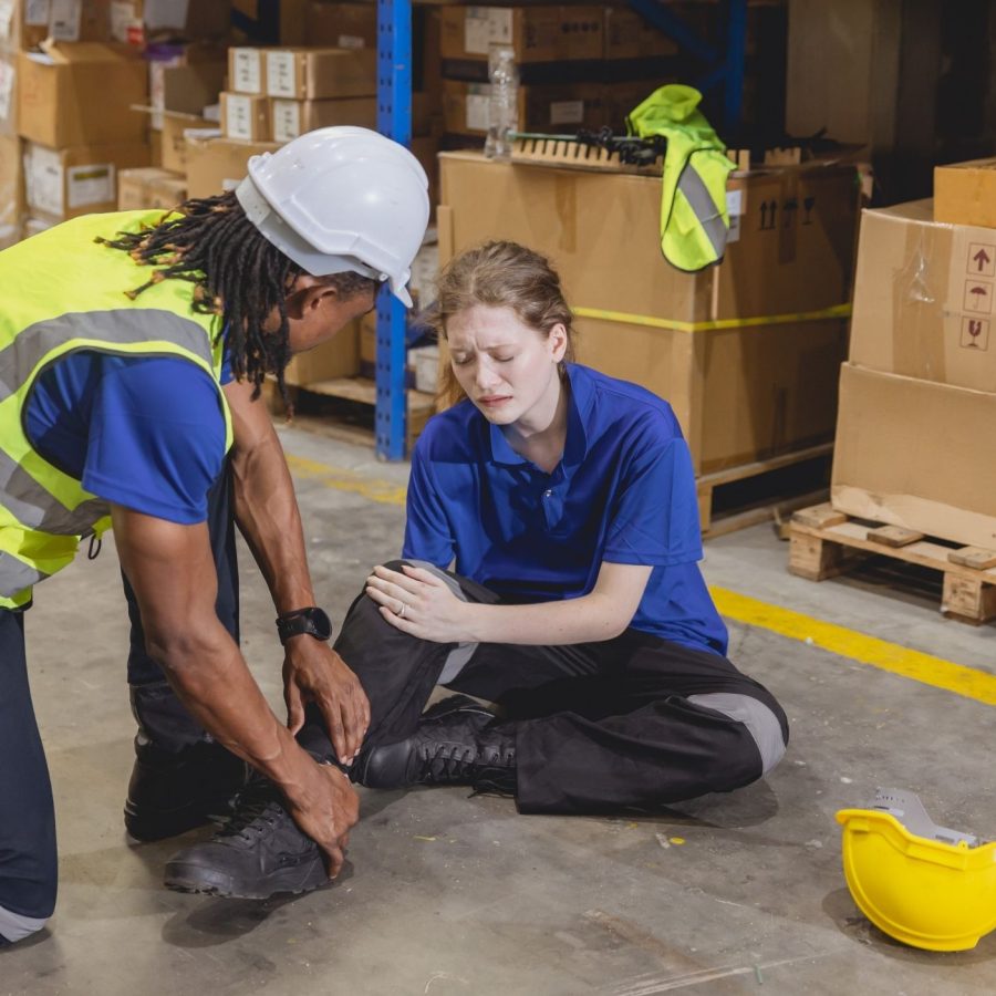 Worker assisting injured colleague in warehouse, highlighting workplace safety concerns and team support.