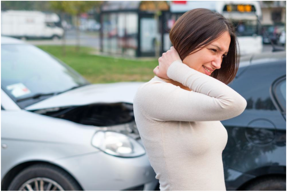 Woman with neck pain after car accident, standing beside two collided cars on street.