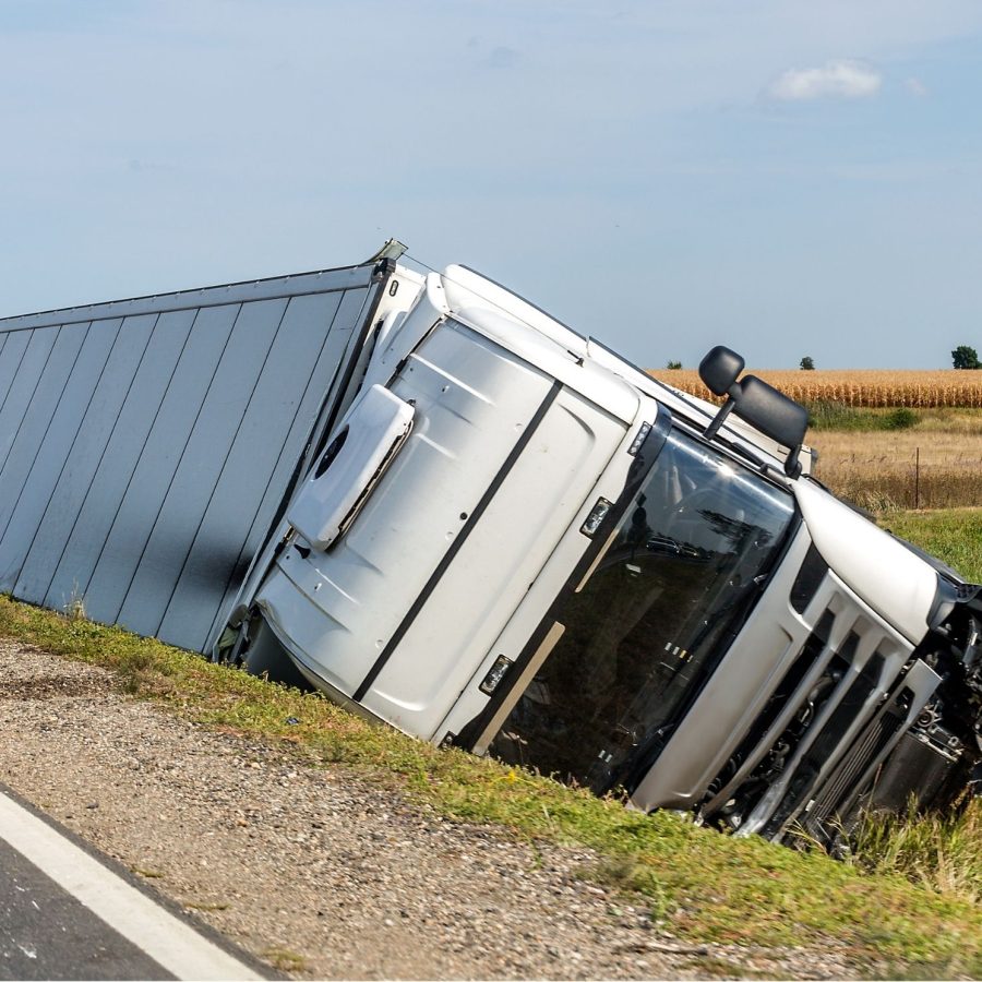 Overturned semi-truck off road in rural area under clear sky, highlighting transportation safety concerns.