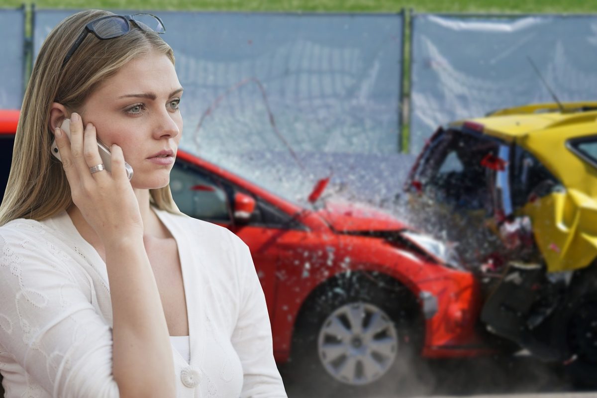 Woman on phone after car accident with red and yellow vehicles, concerned expression.