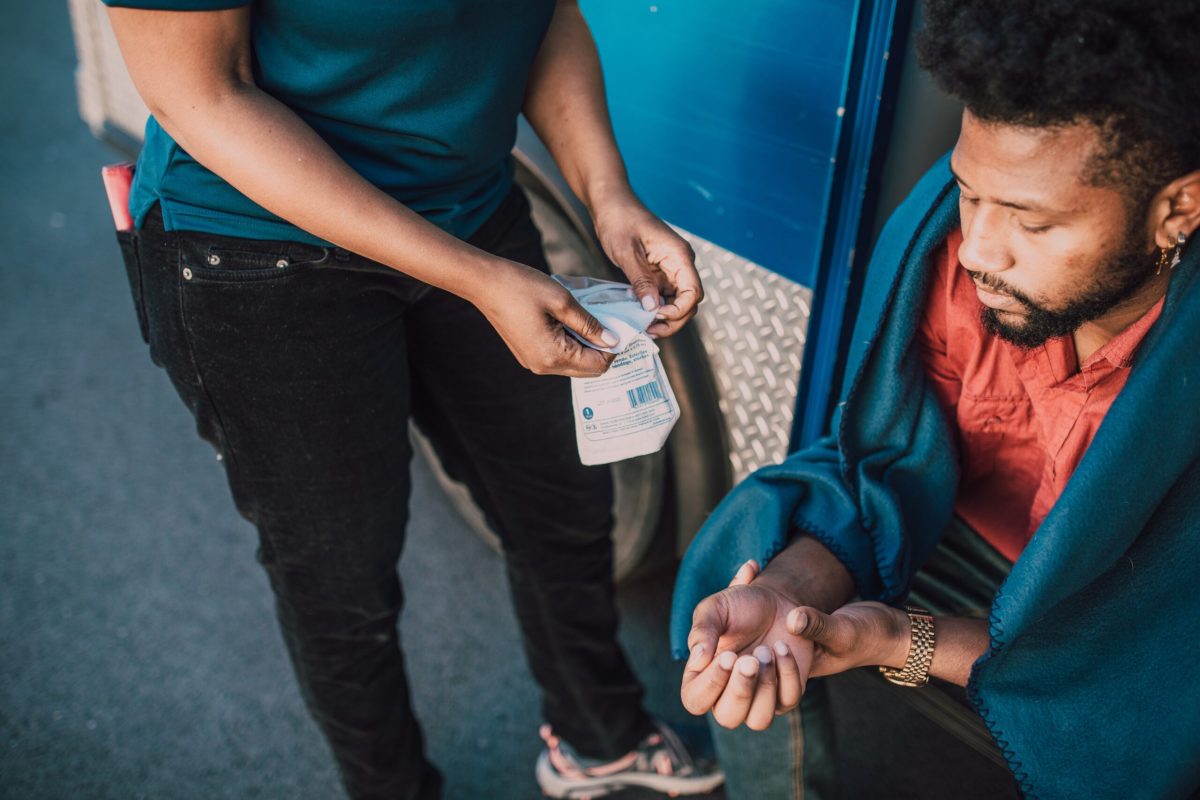 Person offering first aid supplies to another sitting outdoors.