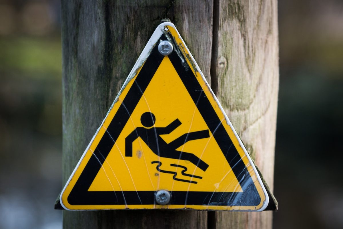 Yellow slippery floor warning sign on wooden post, cautioning about potential hazards.