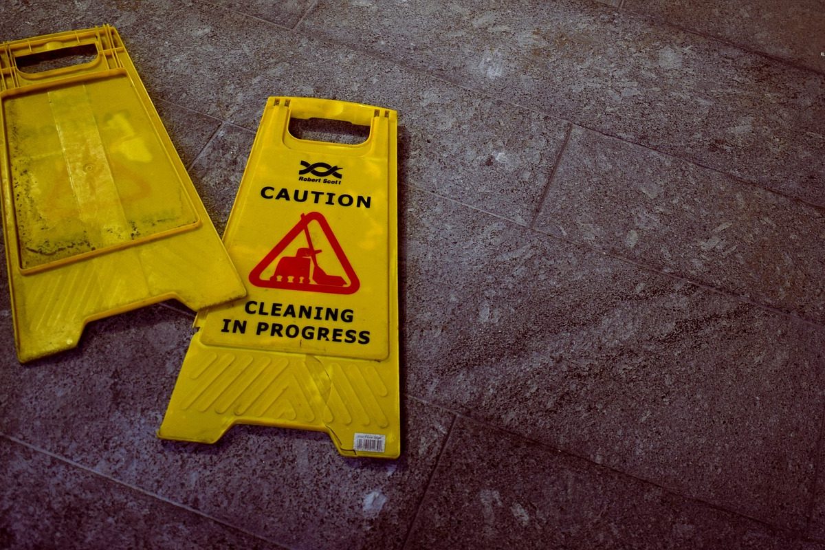 Yellow caution signs on gray tiled floor indicating cleaning in progress.