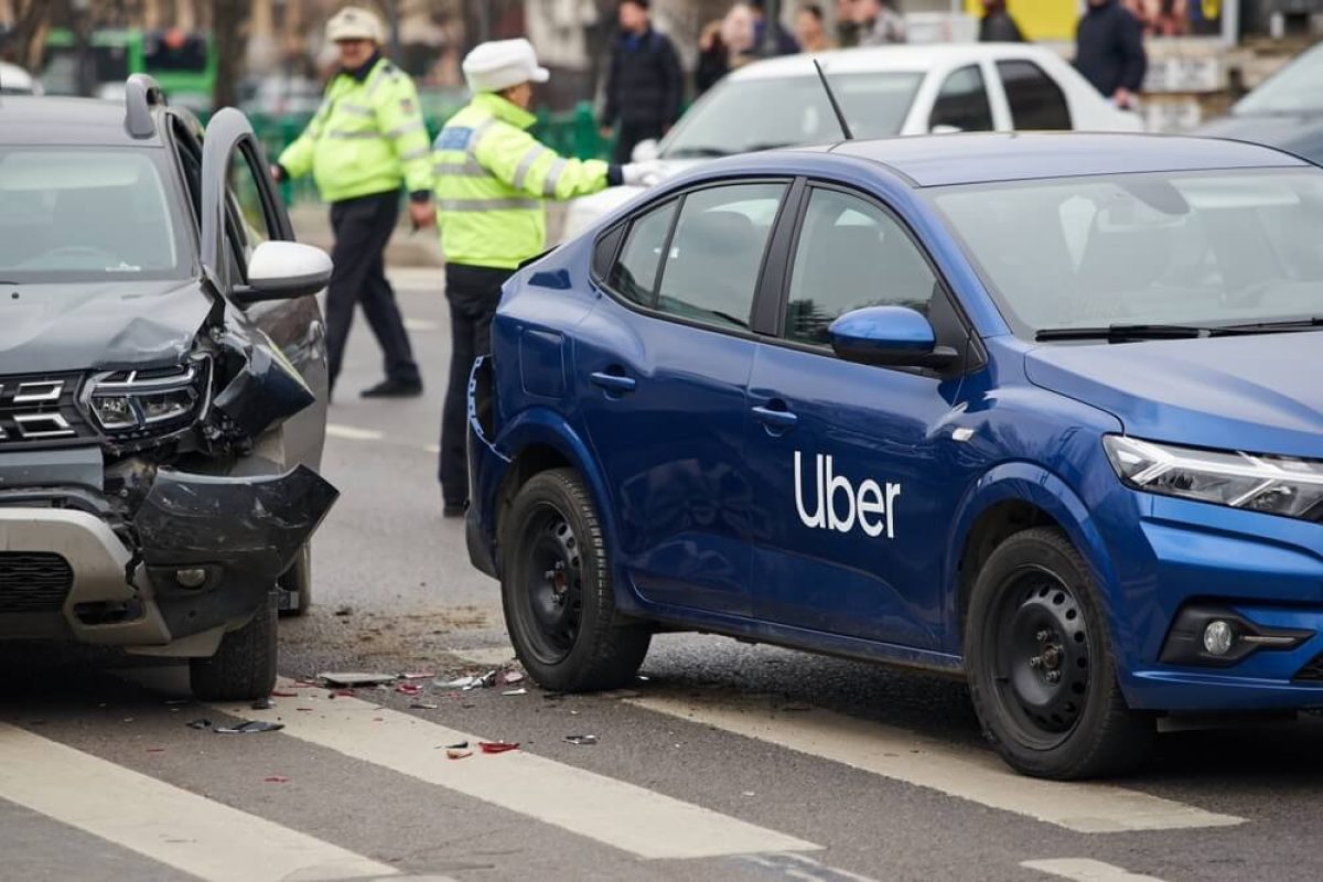 Damaged Uber vehicle at accident scene with first responders arriving, depicting a rideshare crash