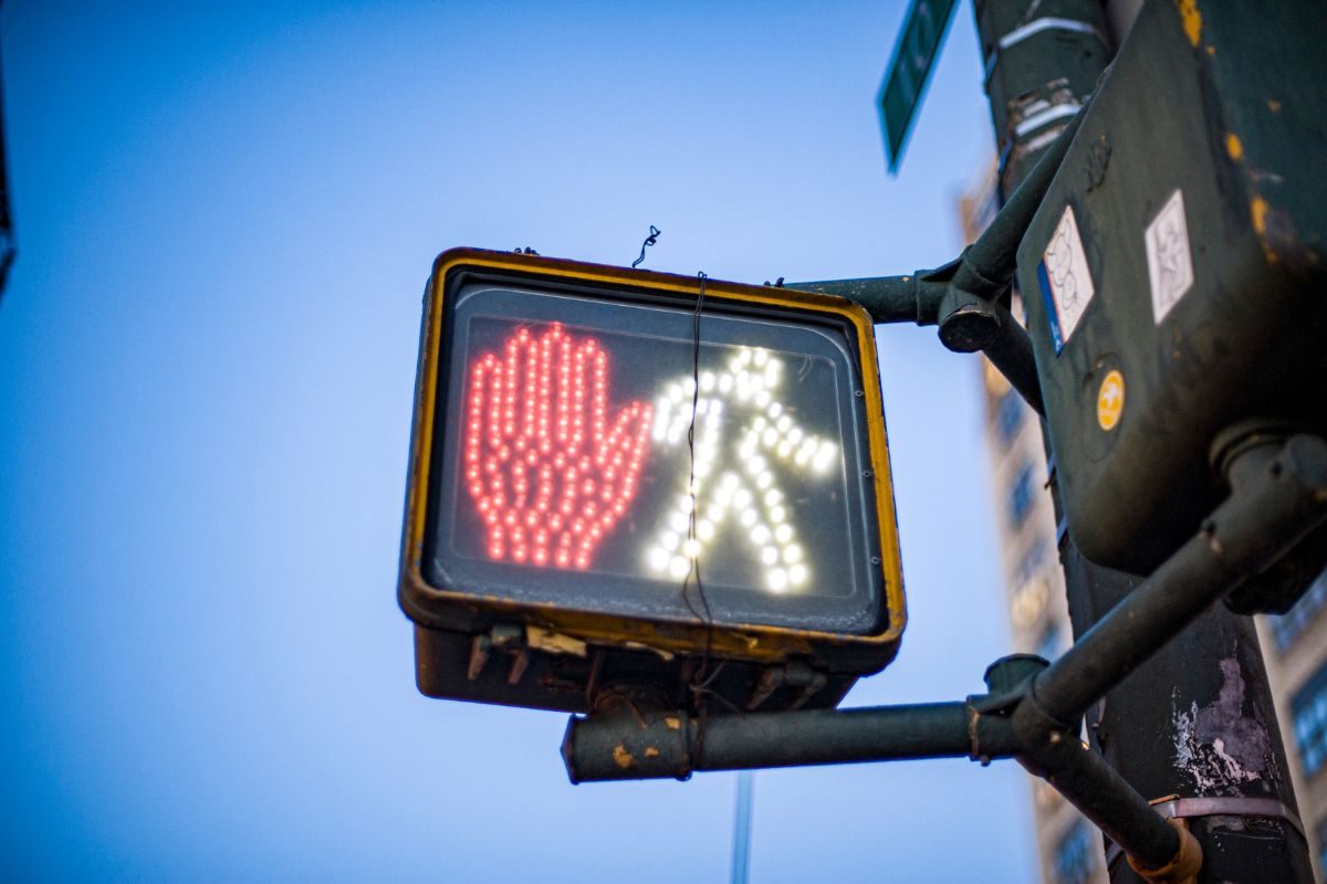 Pedestrian crossing signal showing a red hand and walking figure against a clear blue sky background.